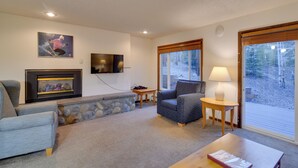 A cozy living room with a fireplace, comfortable seating, a television, and a large window offering a view of the outdoors. - Woodsy Winter Park Condo w/ Pool & Hot Tub Access (Winter Park)
