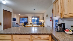 A kitchen with granite countertops, wooden cabinets, a coffee maker, and a dining area with a table and chairs. - Woodsy Winter Park Condo w/ Pool & Hot Tub Access (Winter Park)