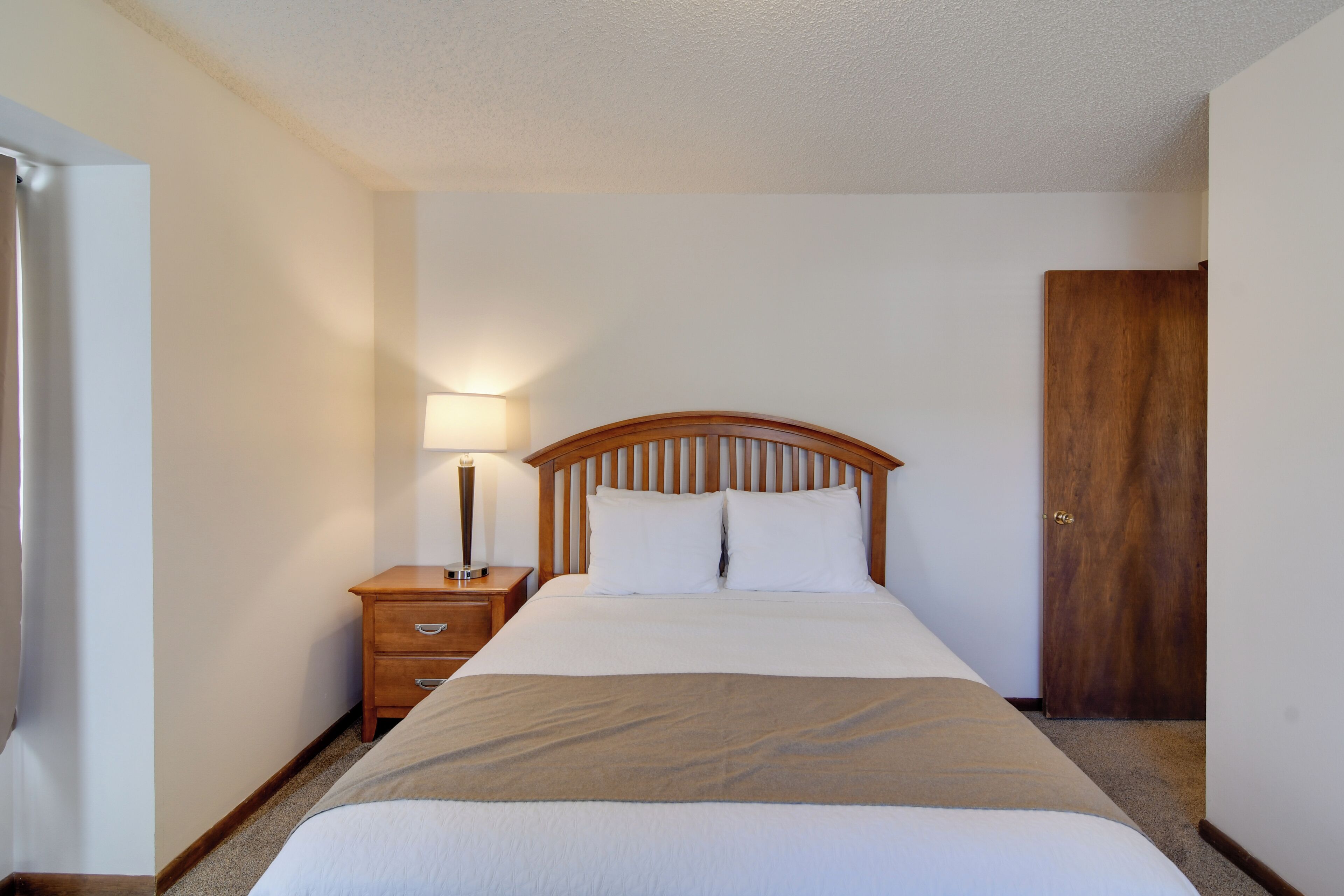 A neatly made bed with a wooden headboard, a bedside lamp, and a wooden nightstand.