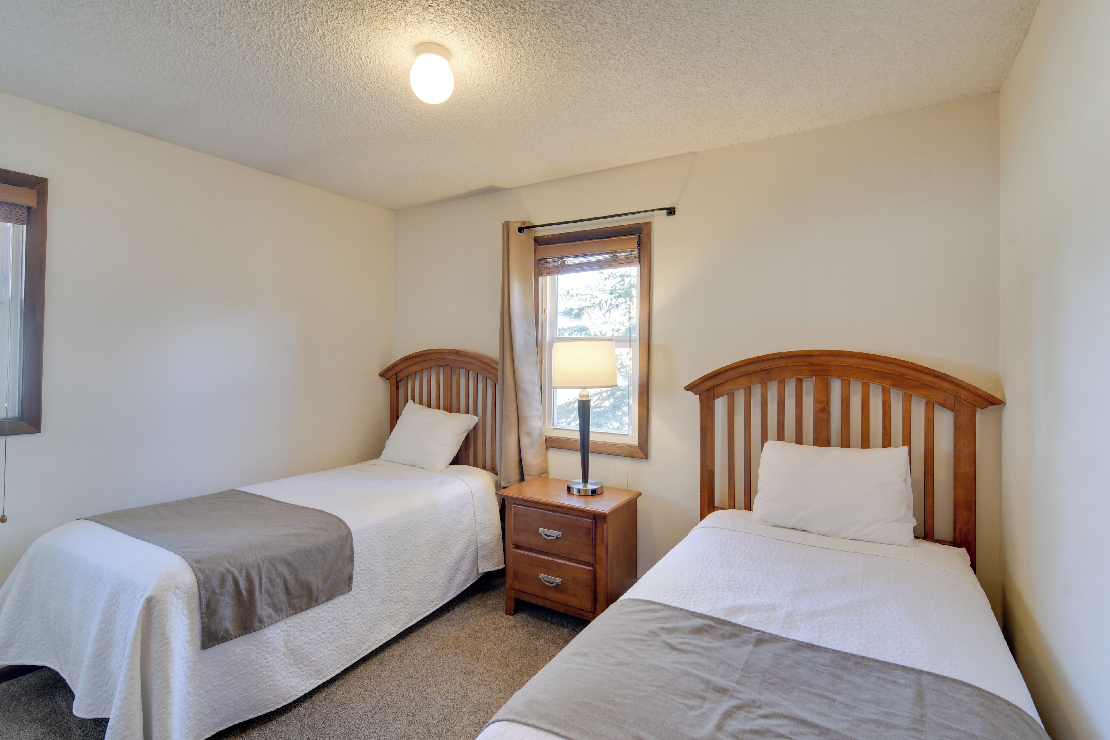 Une chambre avec deux lits simples, une table de chevet avec une lampe et une fenêtre avec des rideaux.