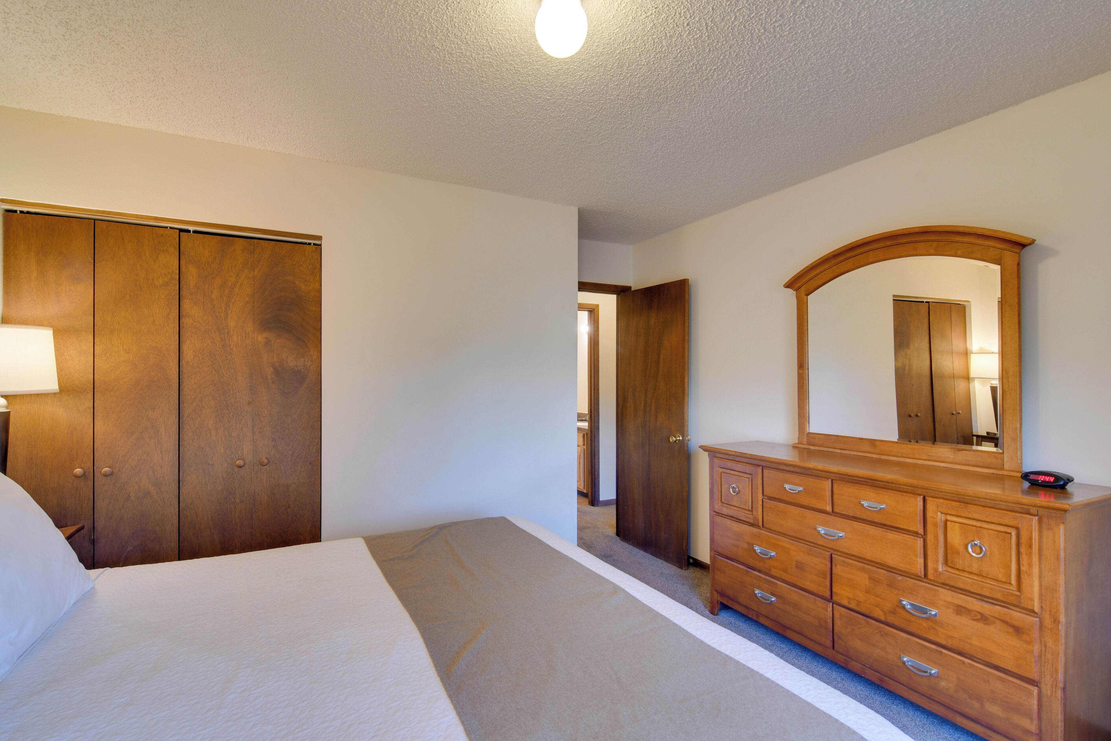 Un dormitorio con una cama grande, un armario de madera, un aparador con cajones y un espejo.