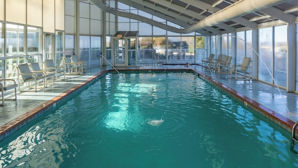 Una piscina interior con agua cristalina, rodeada por paredes de vidrio y barandales de metal.