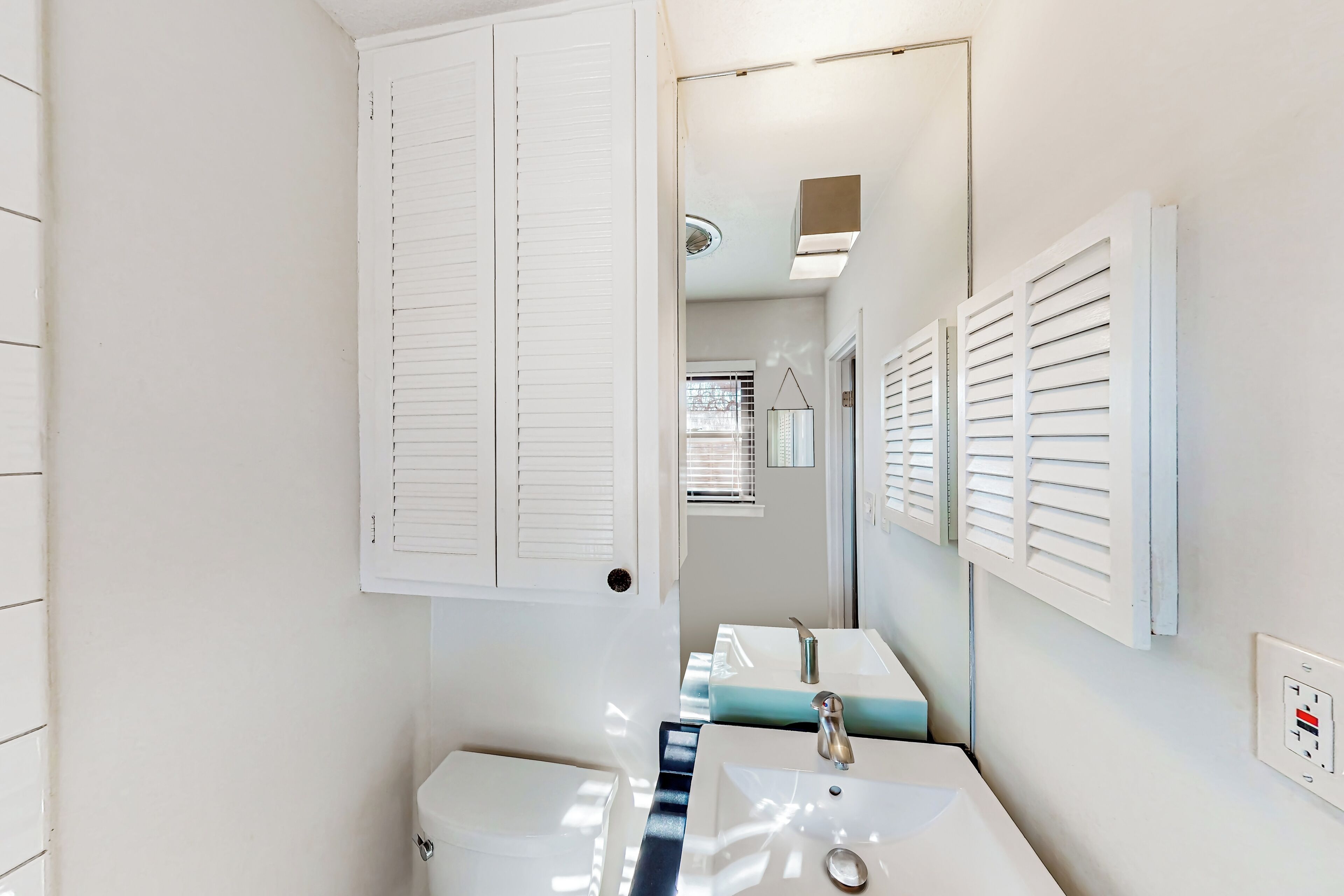 A modern bathroom with white fixtures, a toilet, two sinks, and a mirror.