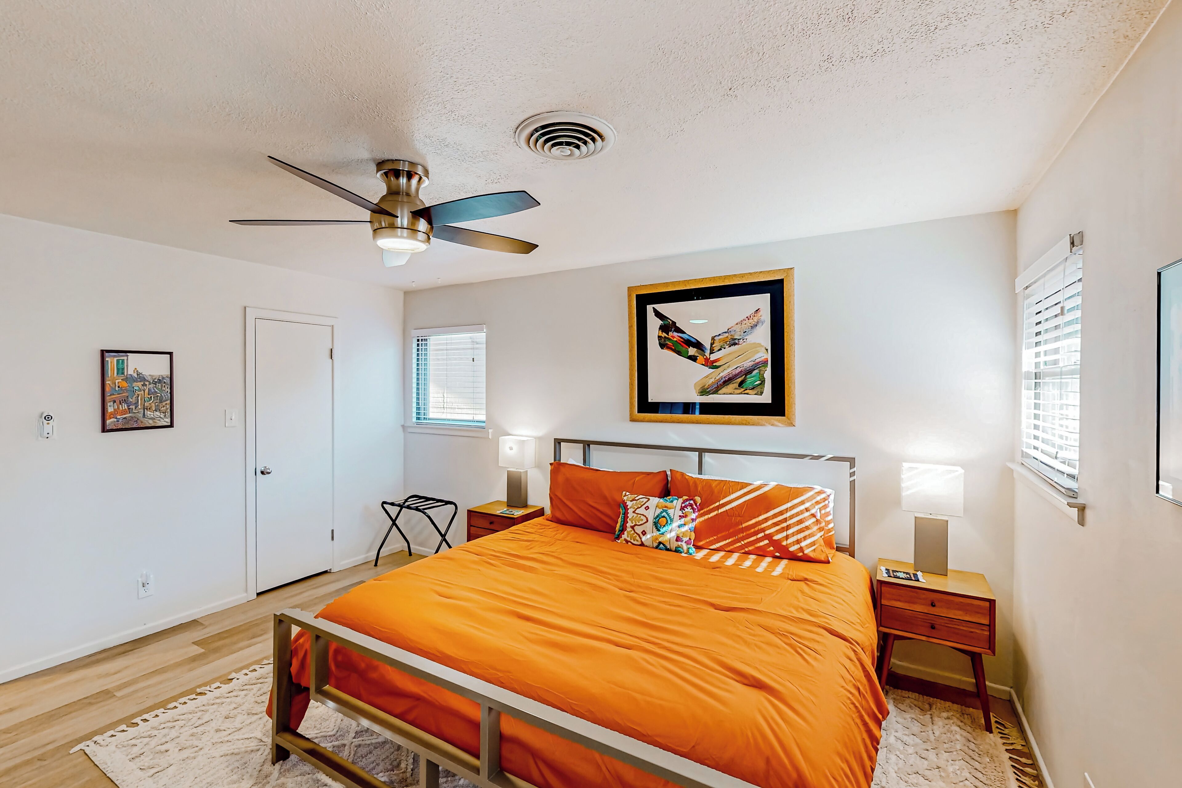 A bedroom with a bed, a ceiling fan, a framed picture, bedside lamps, and a door.