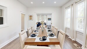 A dining room with a long wooden table, beige chairs, and white walls. - Historic Charm & Great Location! (Augusta)