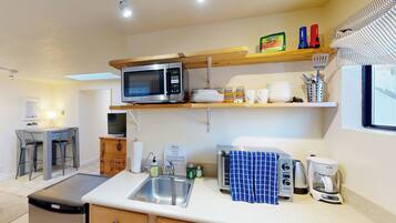 A compact kitchen with a microwave, toaster, coffee maker, and a sink. There are wooden cabinets and a small dining area with a table and chairs.