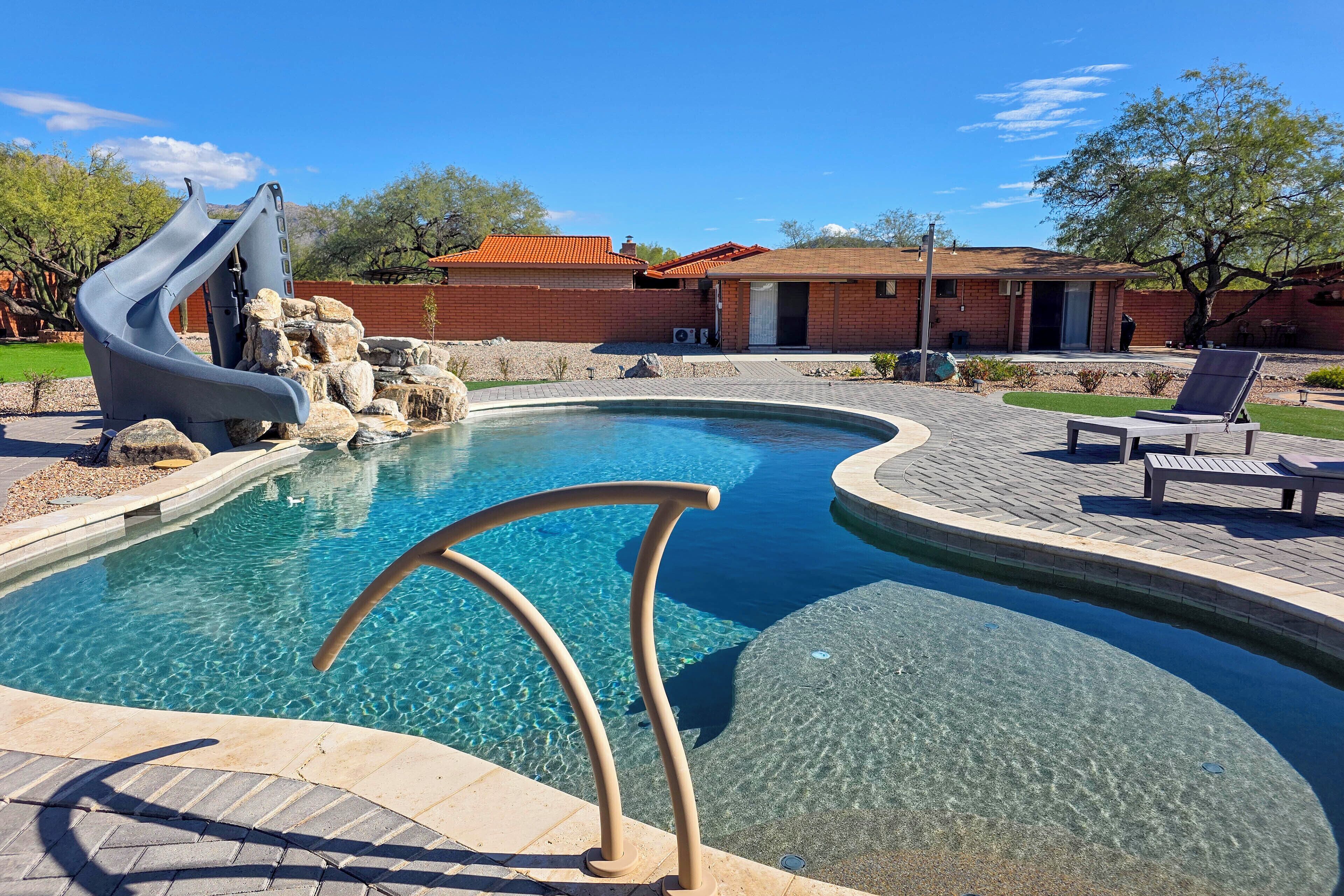A swimming pool with a slide, a brick building, and a tree in the background.