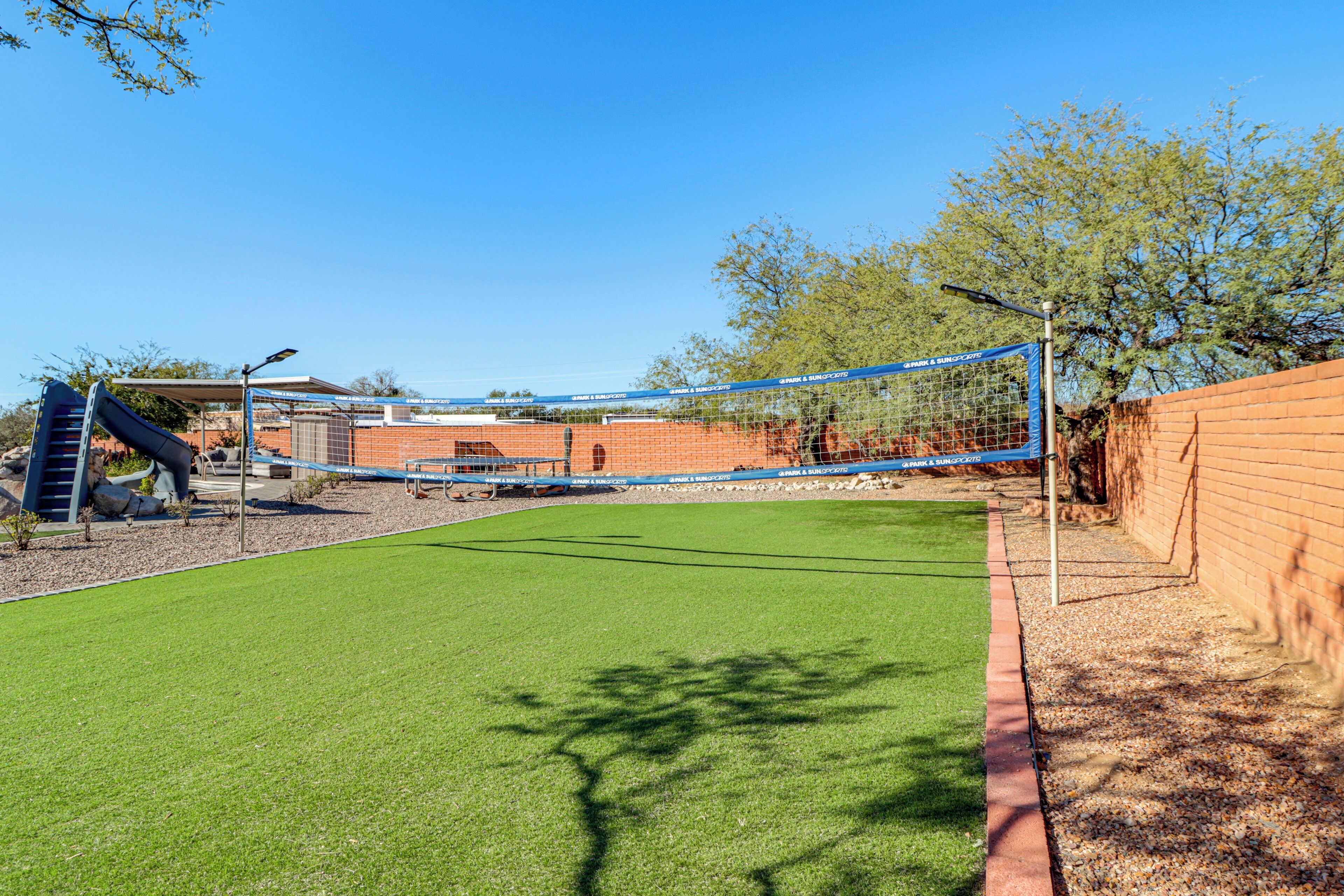 A fenced backyard with artificial grass, a slide, and a brick wall.