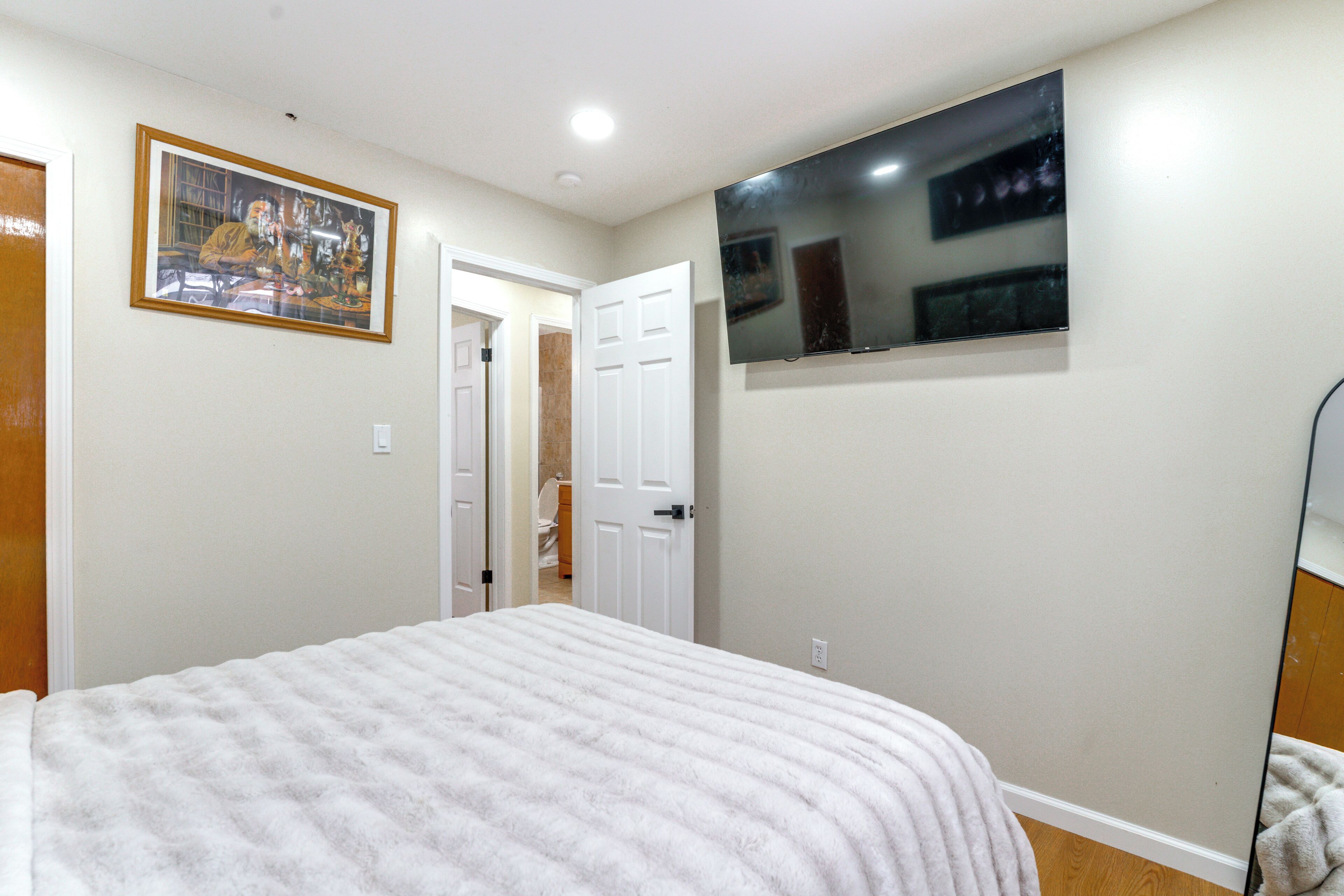 A bedroom with a bed, a door leading to a bathroom, and a TV mounted on the wall.