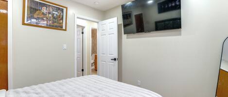 A bedroom with a bed, a door leading to a bathroom, and a TV mounted on the wall.