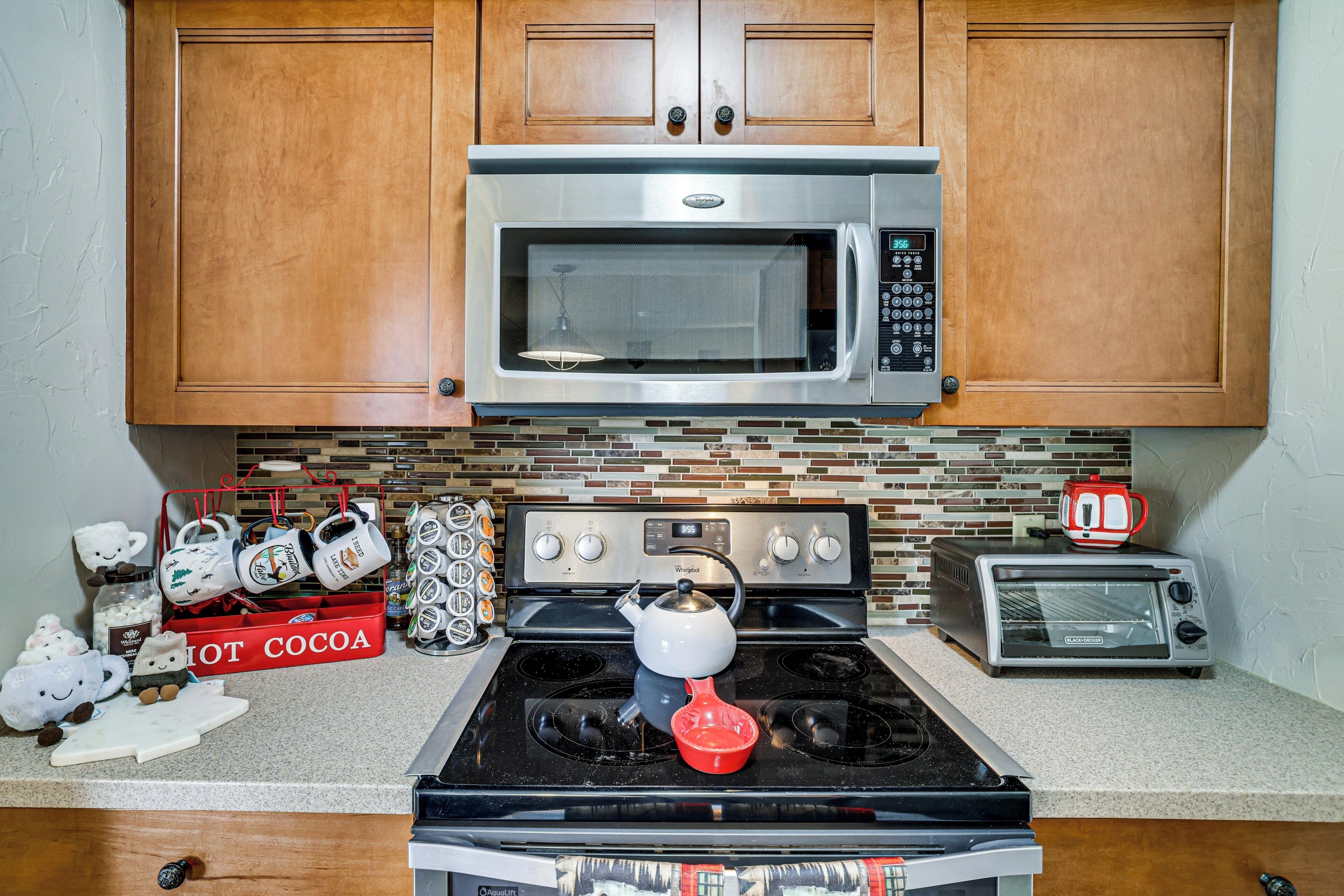 A kitchen with a microwave, stove, toaster, and a 'HOT COCOA' box.