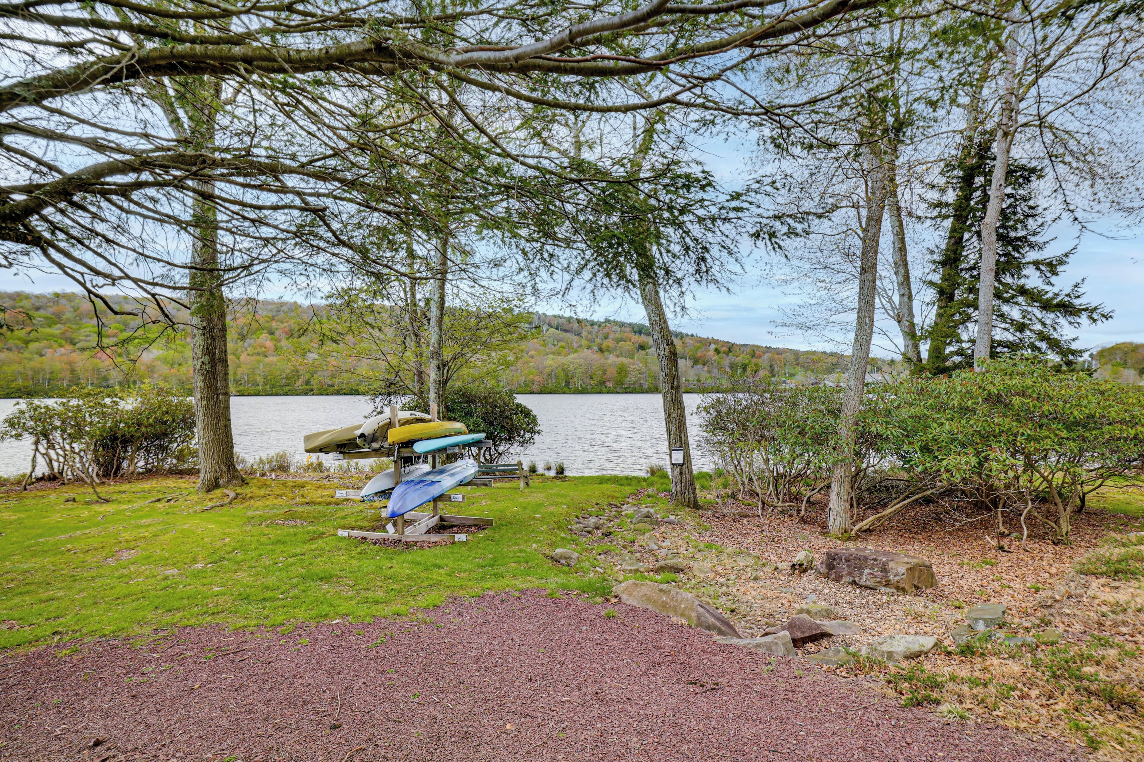 A lakeside camping area with a canoe rack, a picnic table, and a grassy area.