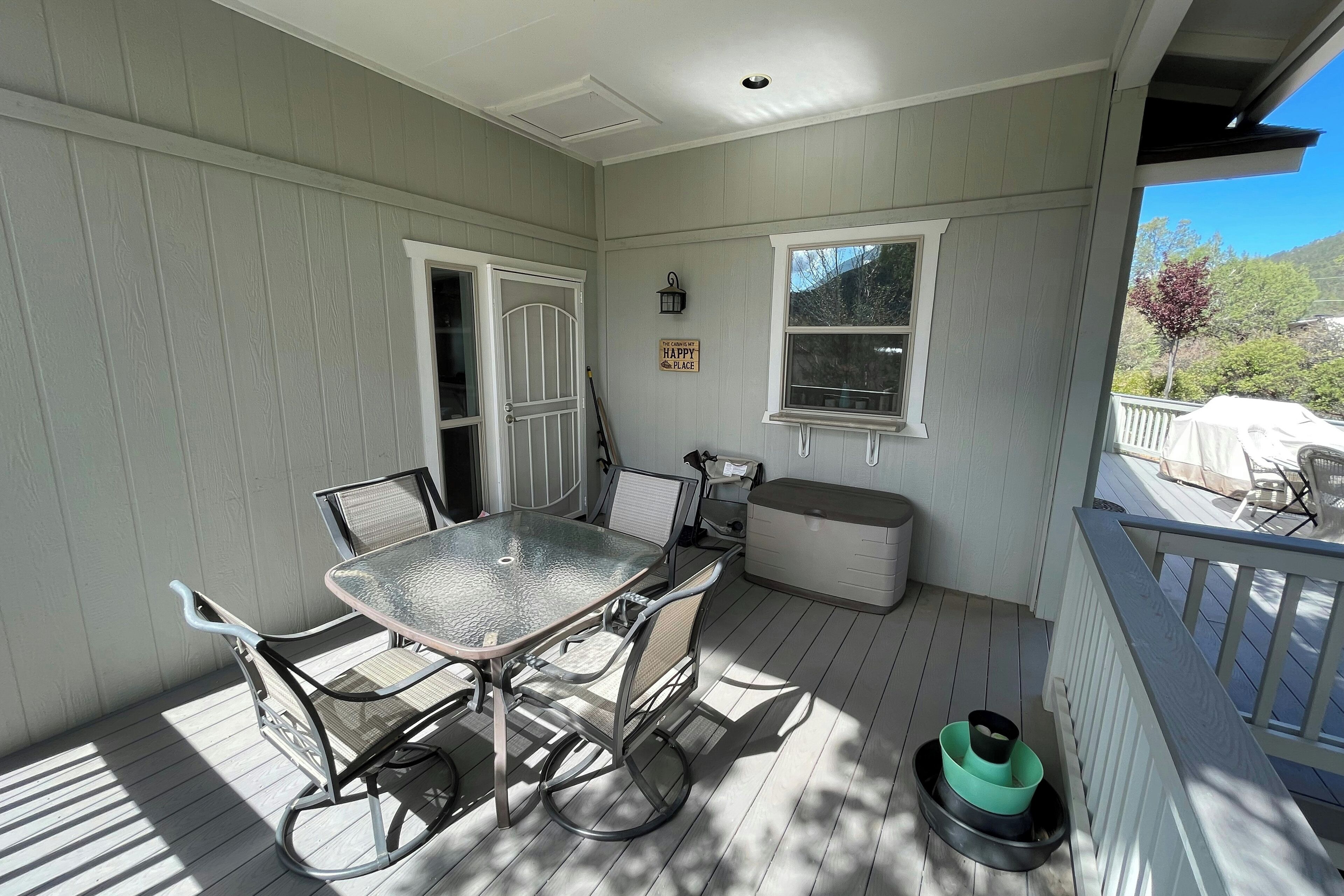 A covered porch with a table and chairs, a bench, a trash can, and a sign that says "HAPPY PLACE".