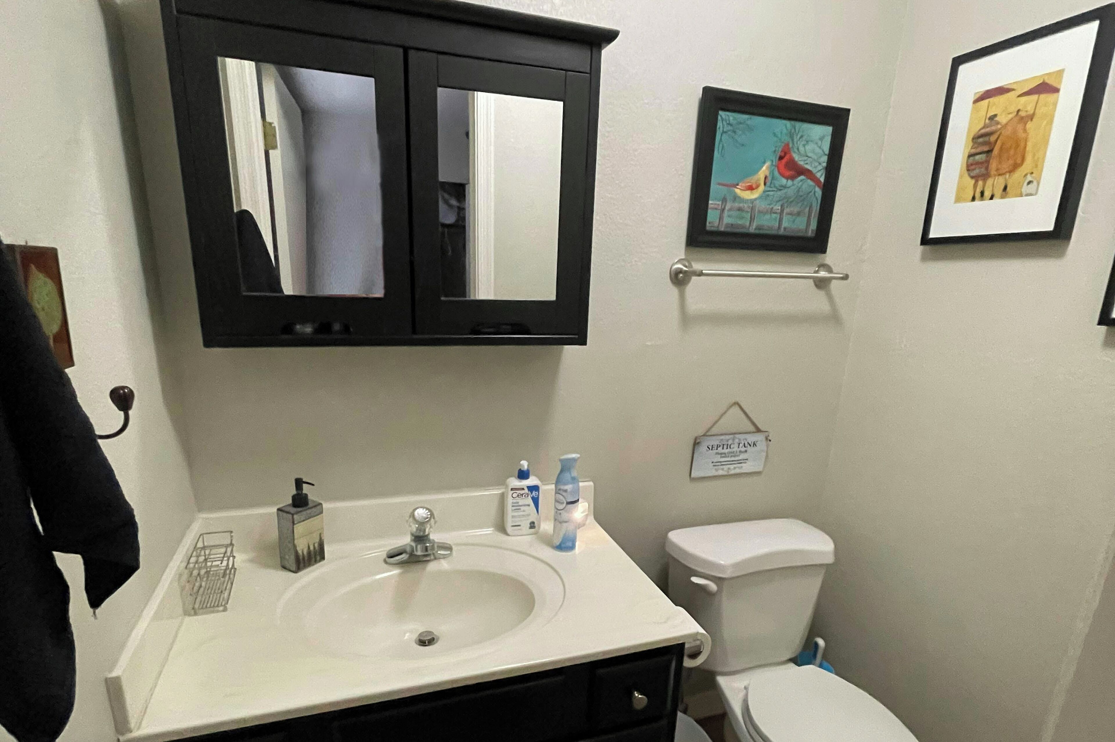 Ein Badezimmer mit einem weißen Waschbecken, einem schwarzen Schrank, einer Toilette und zwei gerahmten Kunstwerken an der Wand.