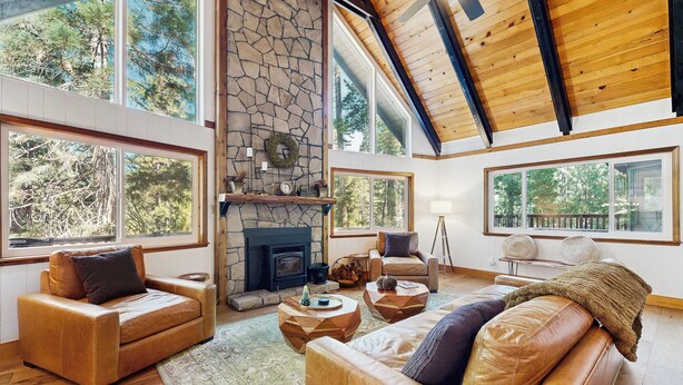 A spacious living room with a stone fireplace, leather sofas, and large windows offering a view of the outdoors. - 4BR Home w/ Spa, Bar, Home Gym, Decks, Near Lake (Arnold)