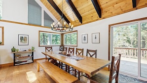 A spacious dining area with a large wooden table and benches, surrounded by large windows offering views of the outdoors. - 4BR Home w/ Spa, Bar, Home Gym, Decks, Near Lake (Arnold)