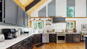 A modern kitchen with dark cabinetry, stainless steel appliances, and a wooden floor. - 4BR Home w/ Spa, Bar, Home Gym, Decks, Near Lake (Arnold)