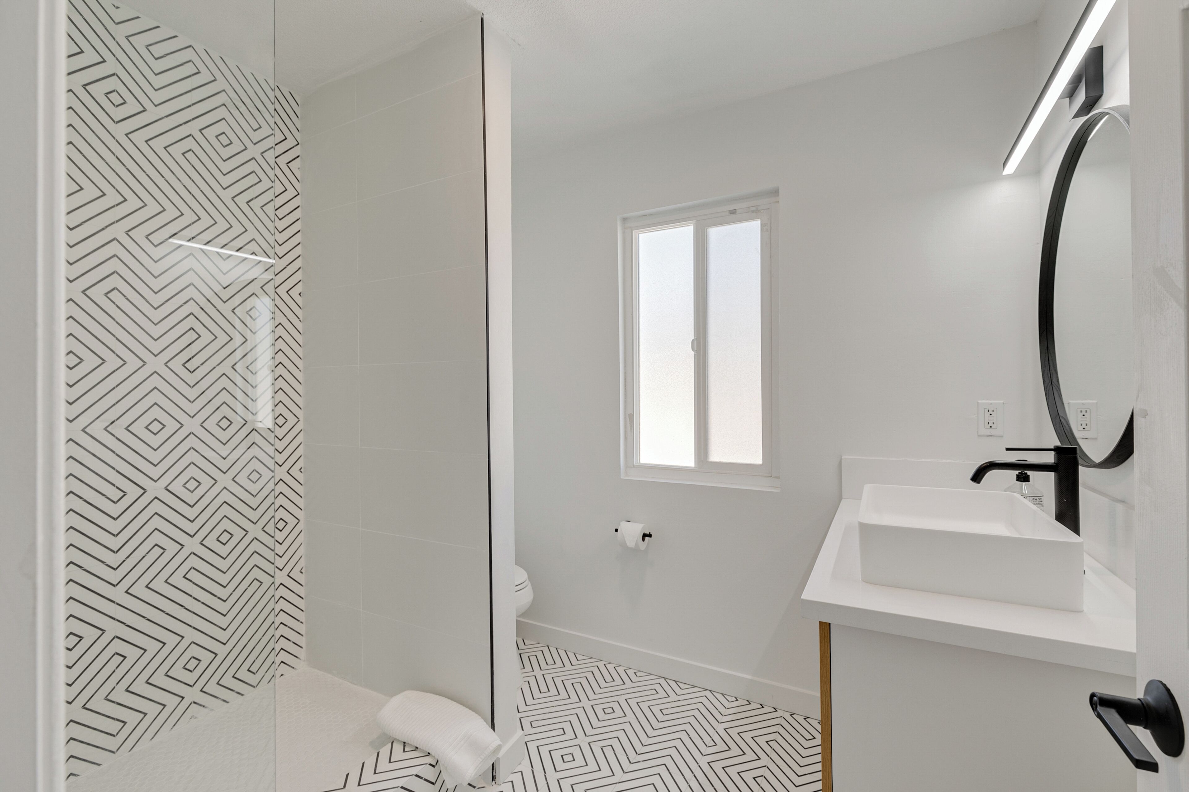 Un baño moderno con piso de patrón geométrico, un lavamanos blanco y una cabina de ducha de vidrio.