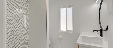 Un baño moderno con piso de patrón geométrico, un lavamanos blanco y una cabina de ducha de vidrio.