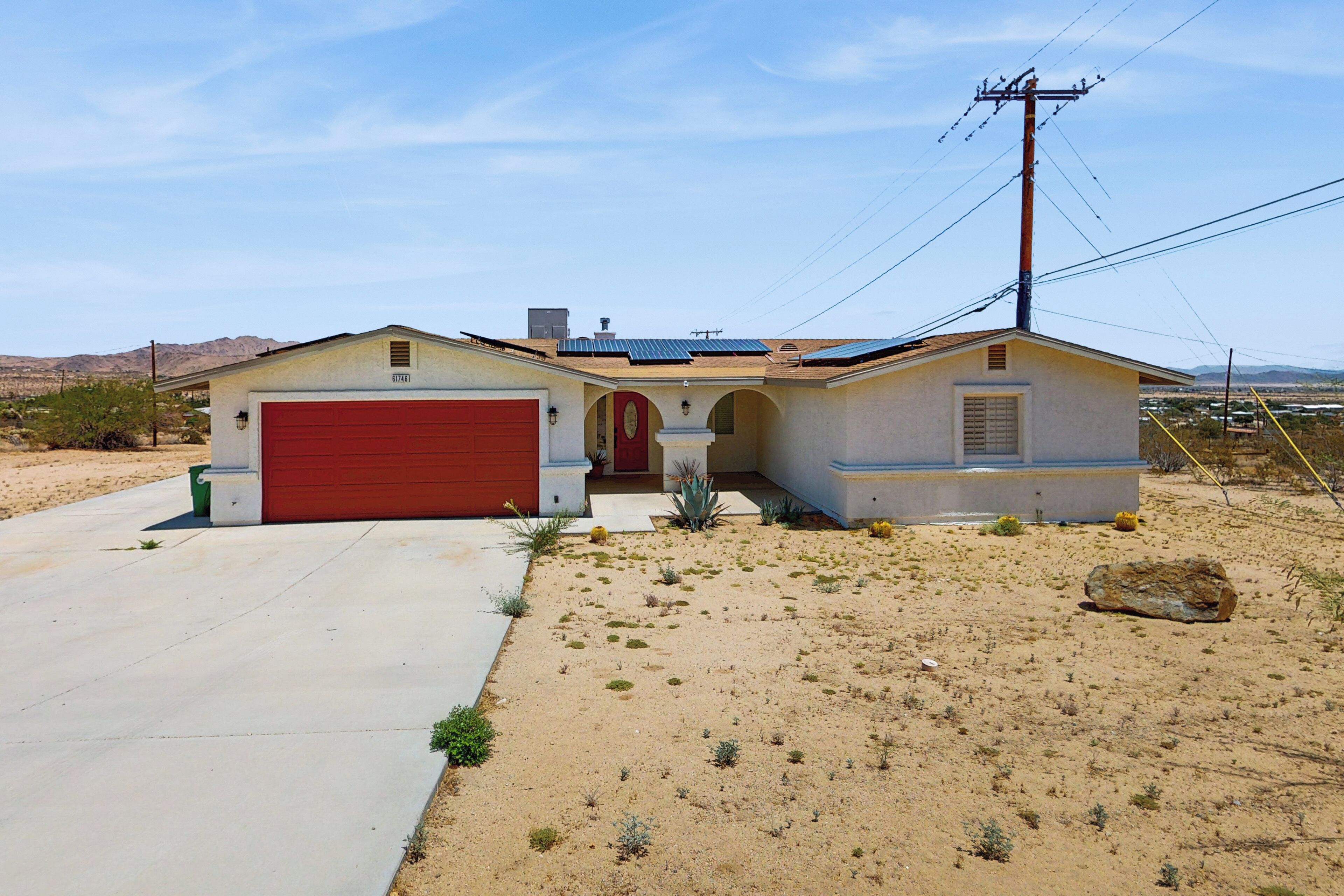A single-story house with a red garage door, a small attached garage, and a solar panel roof.