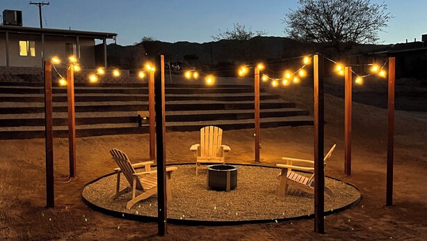 A circular outdoor seating area with wooden chairs and a fire pit, surrounded by a gravel path and wooden posts. - 4BR Home in Joshua Tree w/ Private Pool & Fire Pit (Joshua Tree)