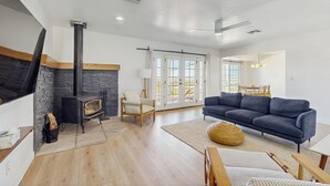 A modern living room with a fireplace, a sofa, and a dining area. - 4BR Home in Joshua Tree w/ Private Pool & Fire Pit (Joshua Tree)