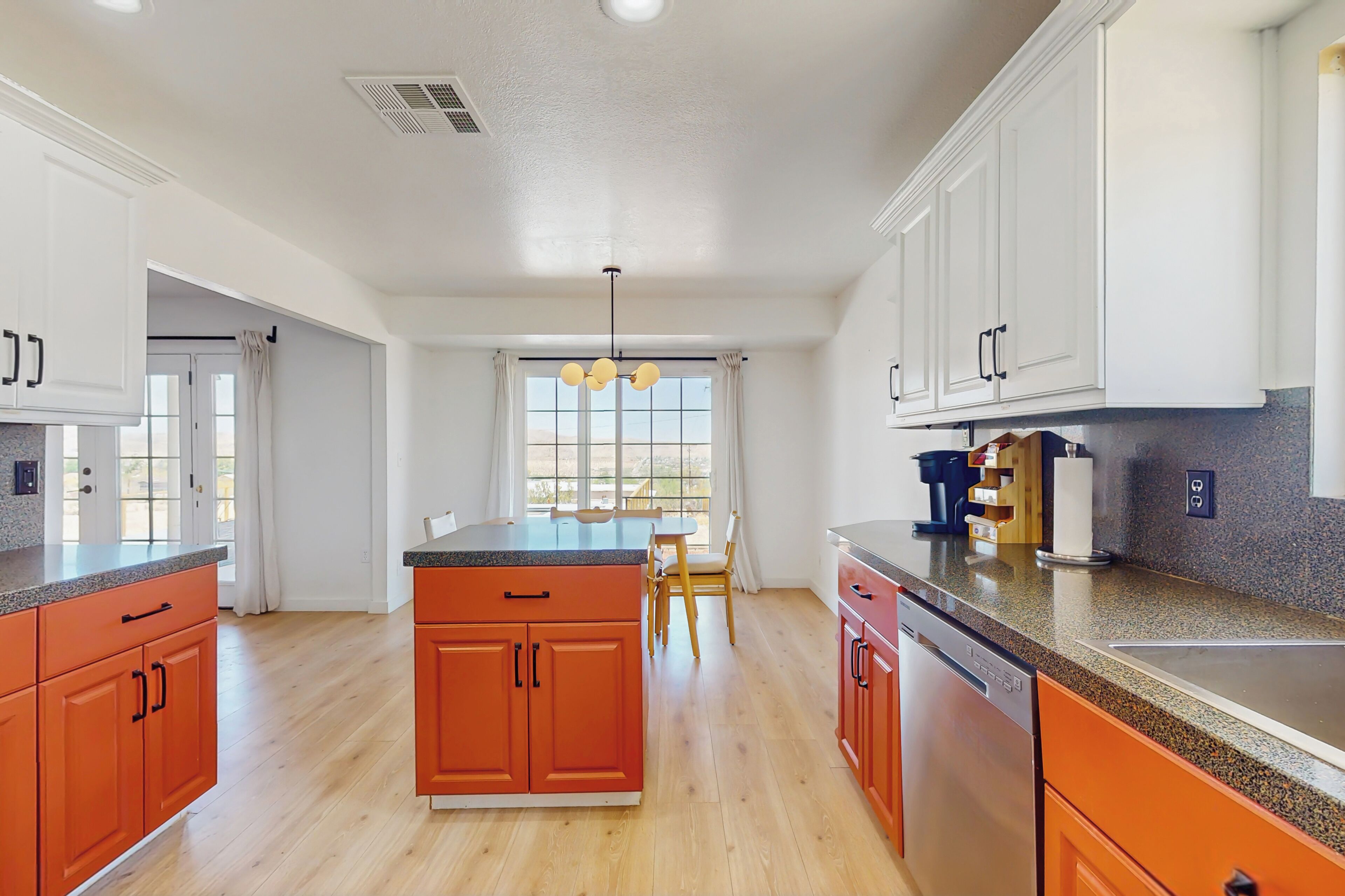 A modern kitchen with white and orange cabinetry, a central island, and a dining area with a view.