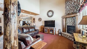 A living room with a stone fireplace, leather sofa, wooden coffee table, and a flat-screen TV. - Steps to Brian Head Resort: Ski Home w/ Games (Brian Head)