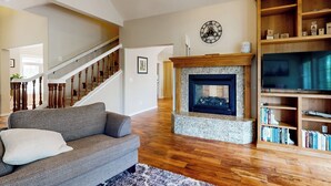A living room with a fireplace, wooden staircase, and a bookshelf. - Hot Tub & Deck! Outdoor Basecamp in Klamath Falls (Klamath Falls)