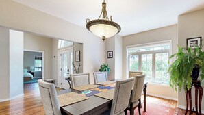 A dining room with a wooden table, six chairs, a chandelier, and a large window. - Hot Tub & Deck! Outdoor Basecamp in Klamath Falls (Klamath Falls)