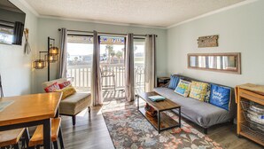 Een gezellige woonkamer met een bank, een houten tafel en een zitbankje. Er is een balkon met uitzicht op palmbomen.