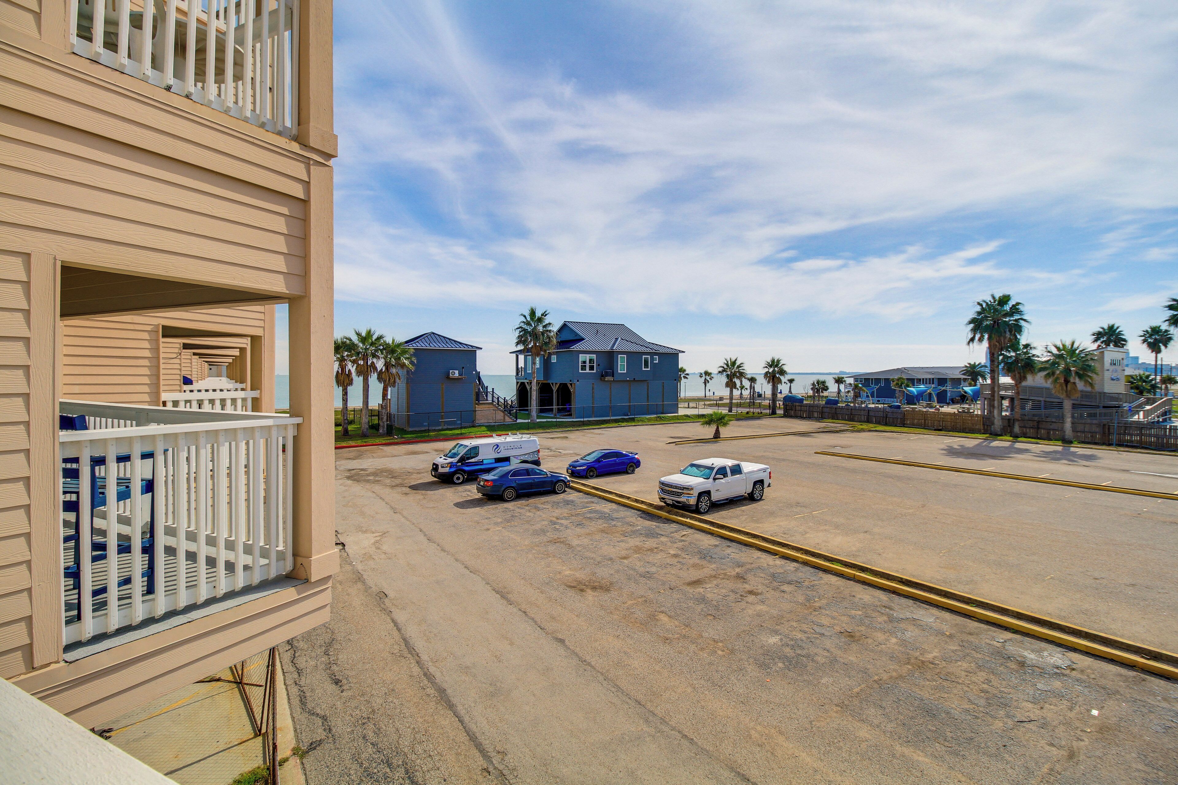 A beachfront property with a parking area, a building with a balcony, and palm trees.