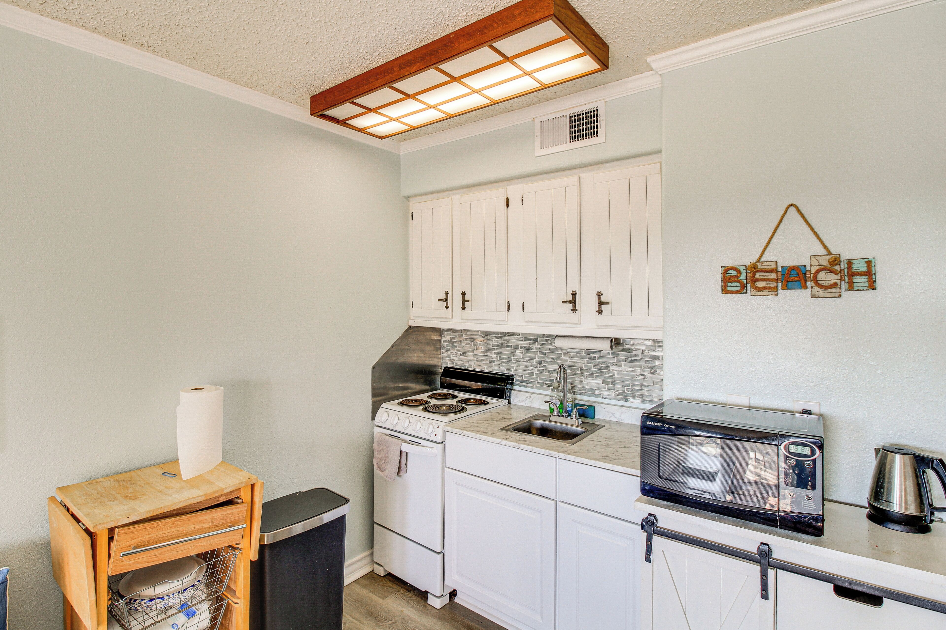 A compact kitchen with white cabinets, a stove, a microwave, and a coffee maker.