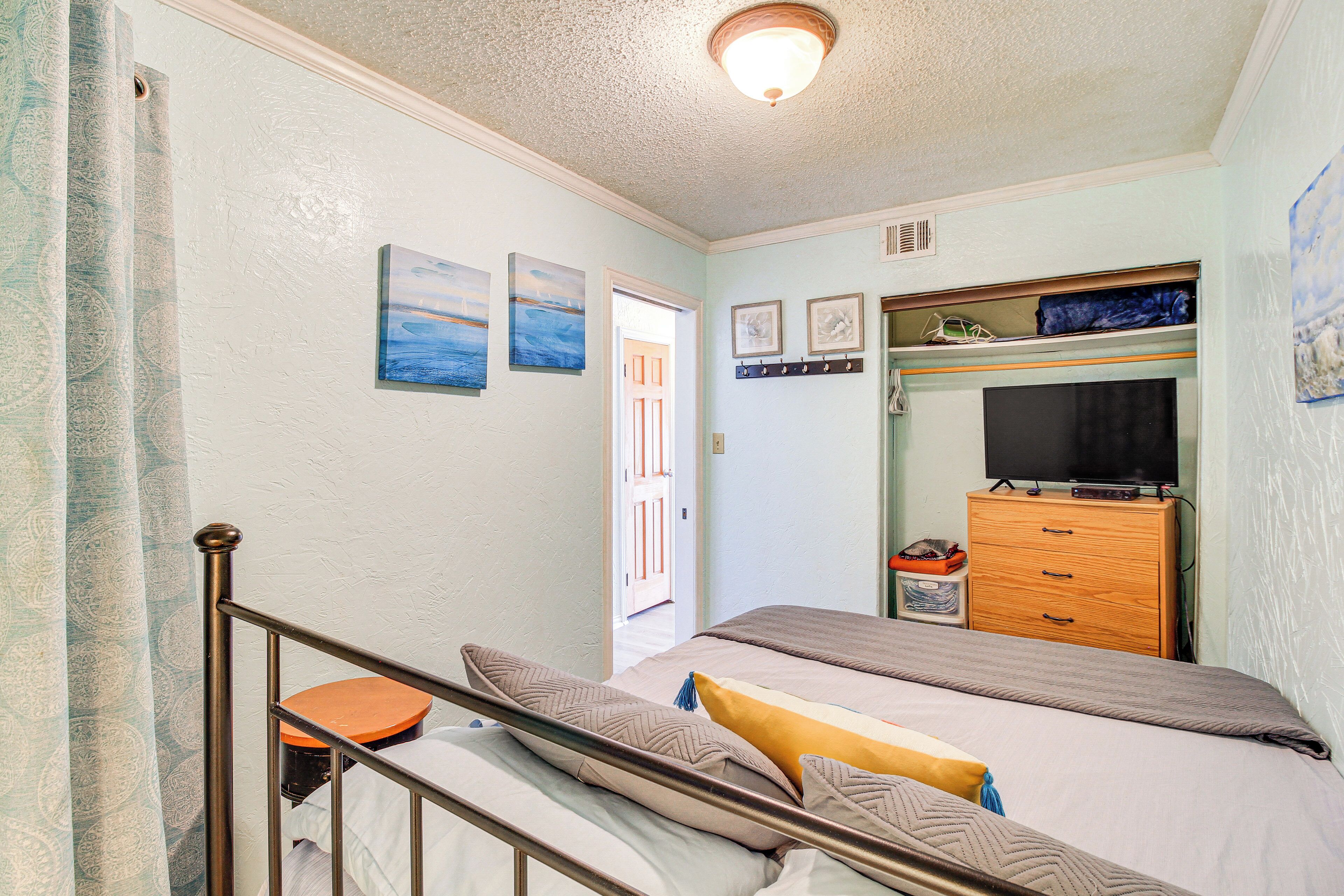 A bedroom with a bed, a dresser, a television, and a door leading to another room.