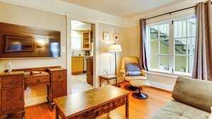 Un salon comprenant un bureau en bois, un canapé, un fauteuil, un téléviseur et une fenêtre avec des rideaux.