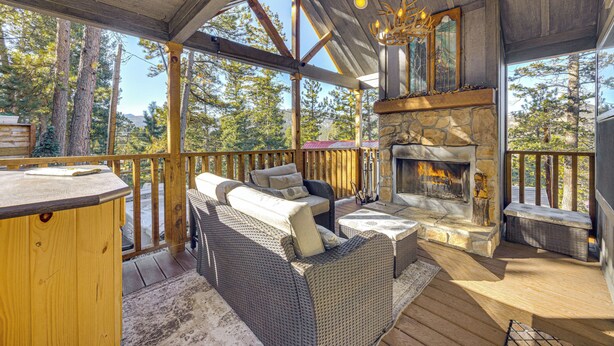 Una terraza de madera con chimenea de piedra, mobiliario de mimbre y vistas al bosque circundante.