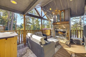 Une terrasse en bois avec une cheminée en pierre, des meubles en osier et une vue sur la forêt environnante.