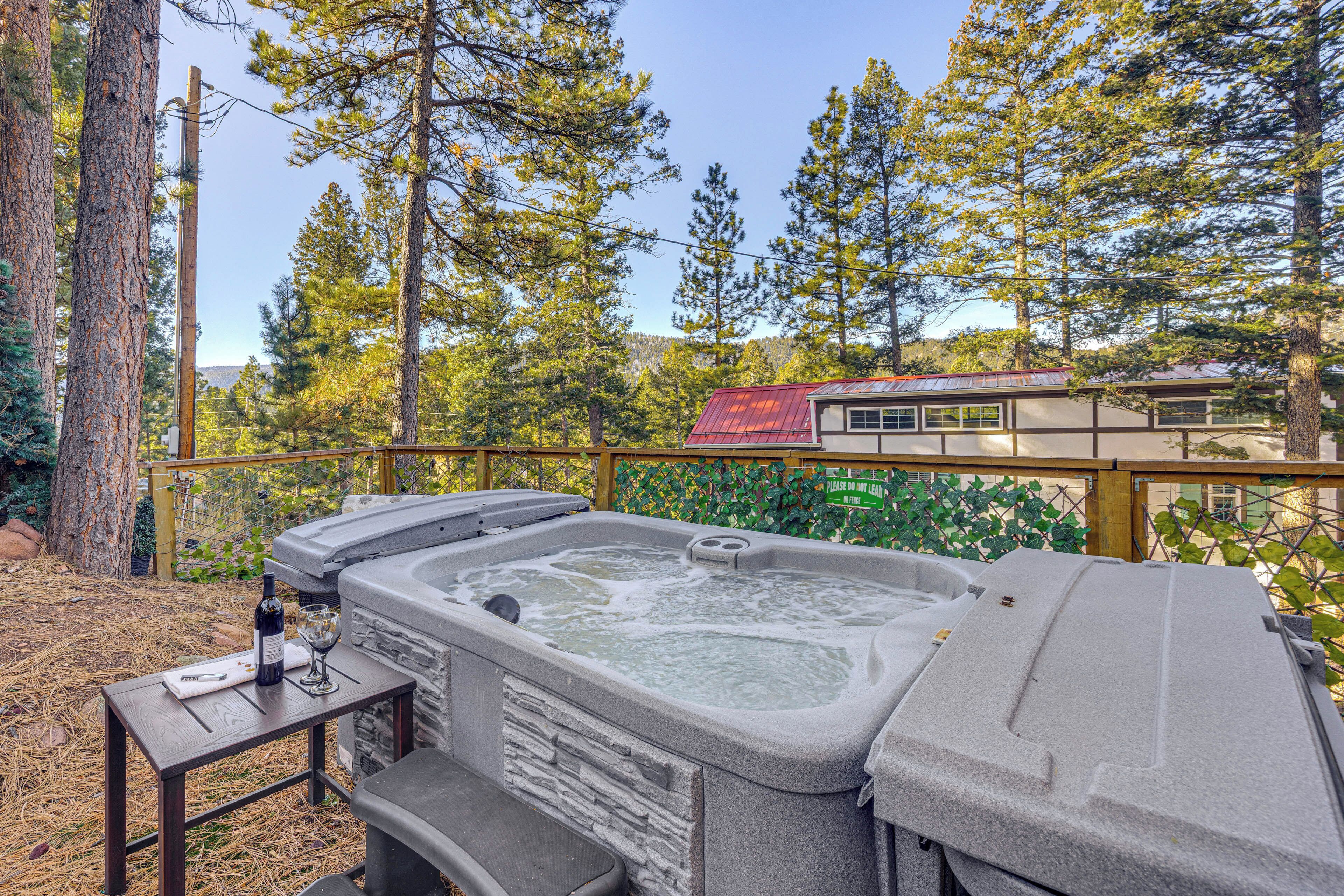 A hot tub with a stone facade, surrounded by a wooden deck and a metal fence.