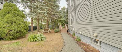 A residential building with a gravel pathway, a picnic table, and various trees.