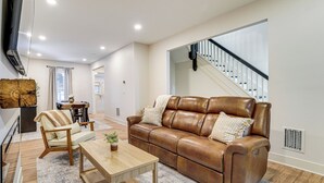 A modern living room with a brown leather sofa, wooden coffee table, and a dining area with a table and chairs. - Game Room & Backyard: Modern Altoona Home! (Altoona)