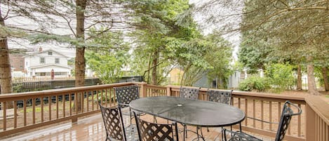 A wooden deck with a round table and chairs, surrounded by trees and a fence.