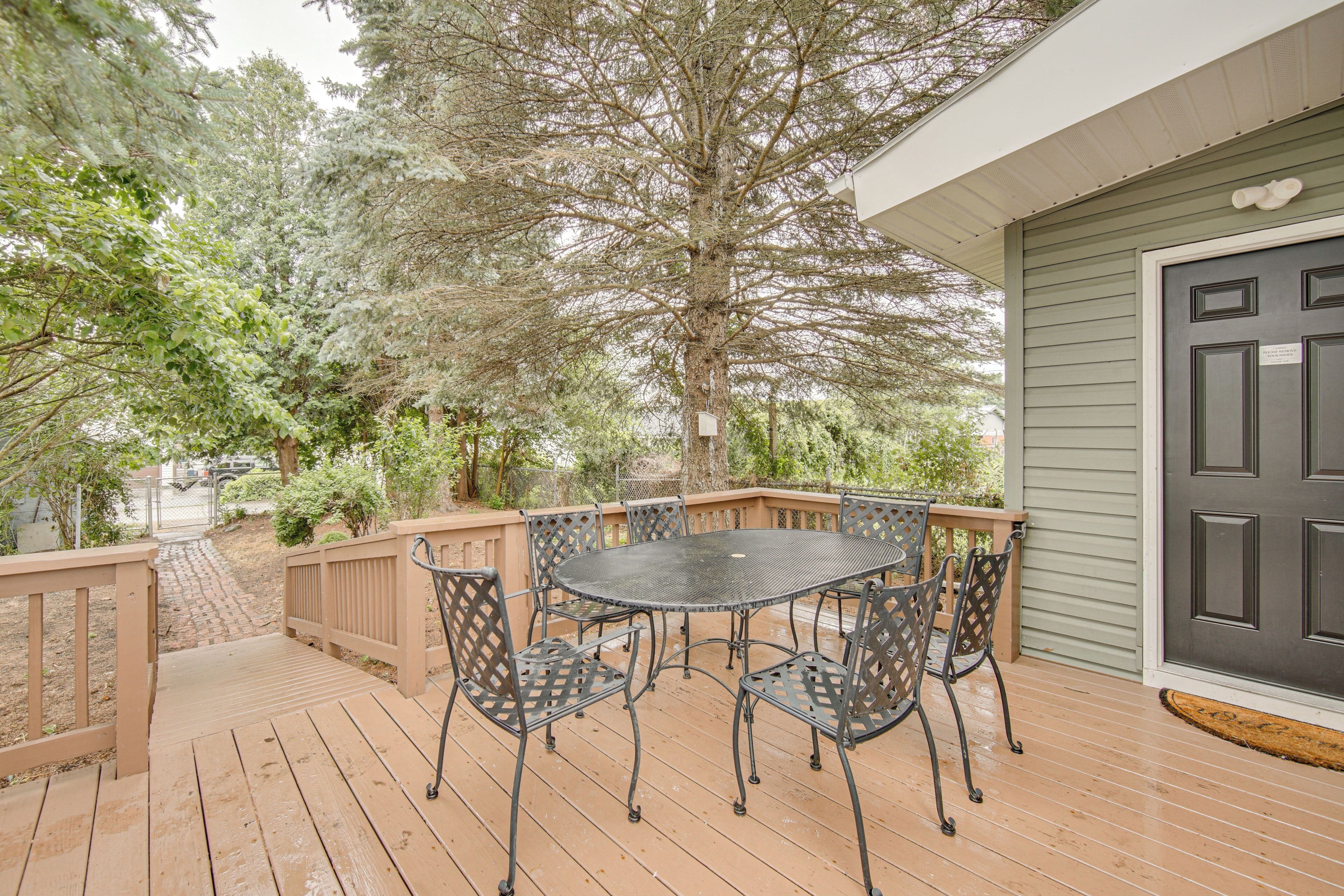 A wooden deck with a round table and chairs, a dark door, and a tree in the background.