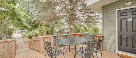 A wooden deck with a round table and chairs, a dark door, and a tree in the background.