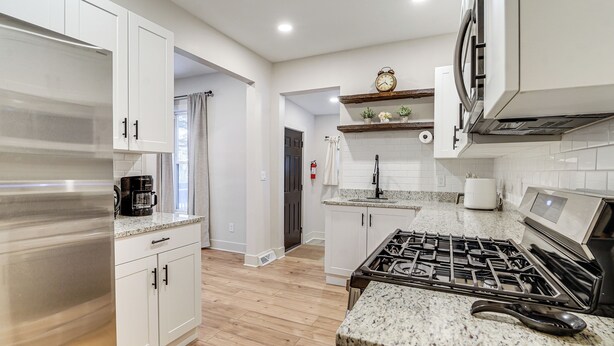 A modern kitchen with white cabinets, a stainless steel refrigerator, a gas stove, and a coffee maker. - Game Room & Backyard: Modern Altoona Home! (Altoona)