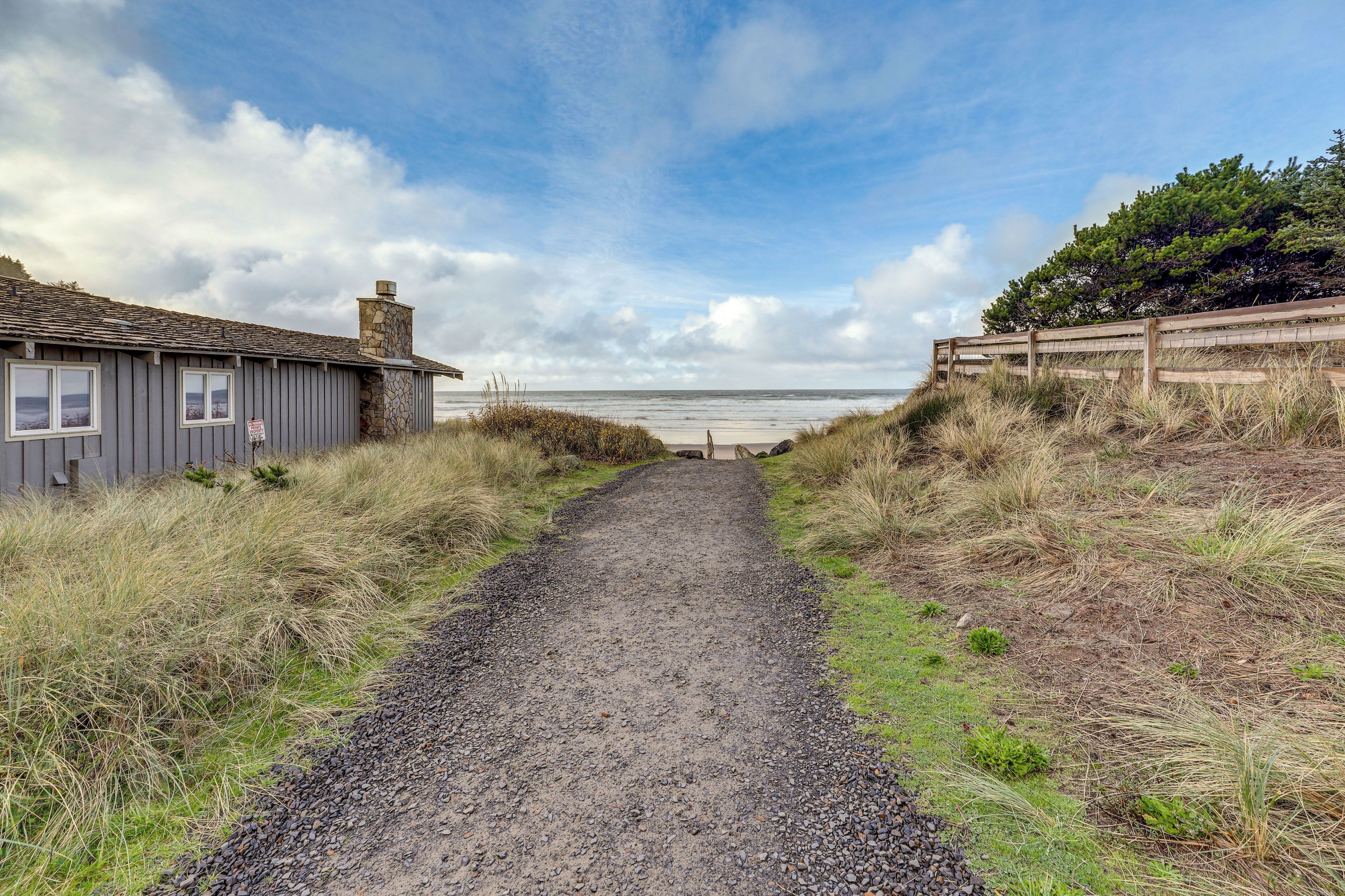 A gravel path leading to a beach with a wooden fence on one side and a building on the other.