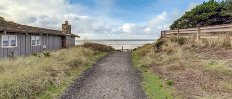 A gravel path leading to a beach with a wooden fence on one side and a building on the other.