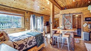 A wooden cabin with a bed, a dining area with stools, and a TV. - Walk to Main Street! Mtn-view Getaway in Pioche (Pioche)
