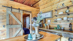 A wooden interior with a kitchen area, including a wooden table with a vase of flowers, a sink, and shelves with dishes and utensils. - Walk to Main Street! Mtn-view Getaway in Pioche (Pioche)