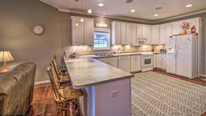 A modern kitchen with white cabinets, a central island, and a dining area with a brown leather couch and wooden chairs. - Boat Dock: Lake-view Retreat 5 Mi to Dtwn Clemson (Seneca)