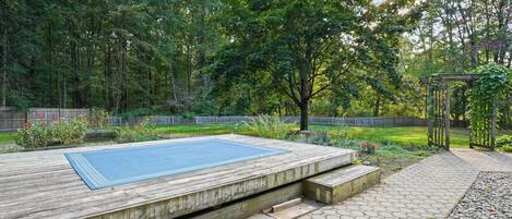 A wooden deck with a blue mat, hexagonal stone tiles, and a pergola with climbing plants.